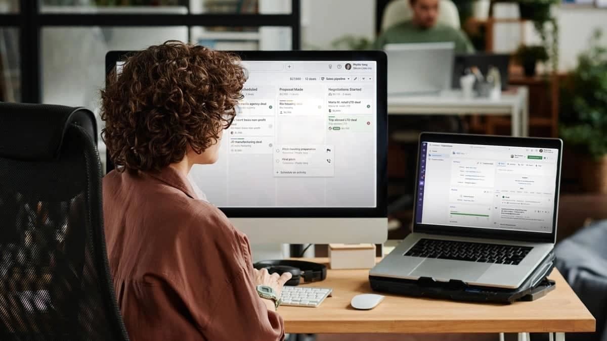 A female sales professional reviewing an AI-powered sales pipeline and CRM dashboard on dual screens.